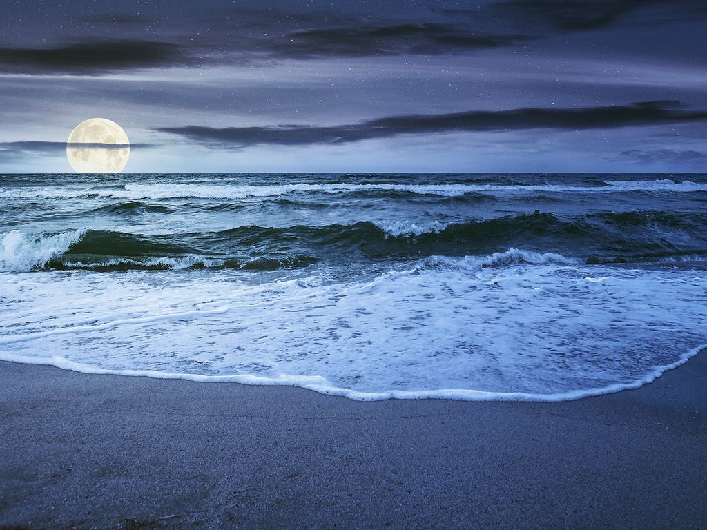 Foto de las mareas del océano subiendo en la playa, con la Luna detrás del horizonte.