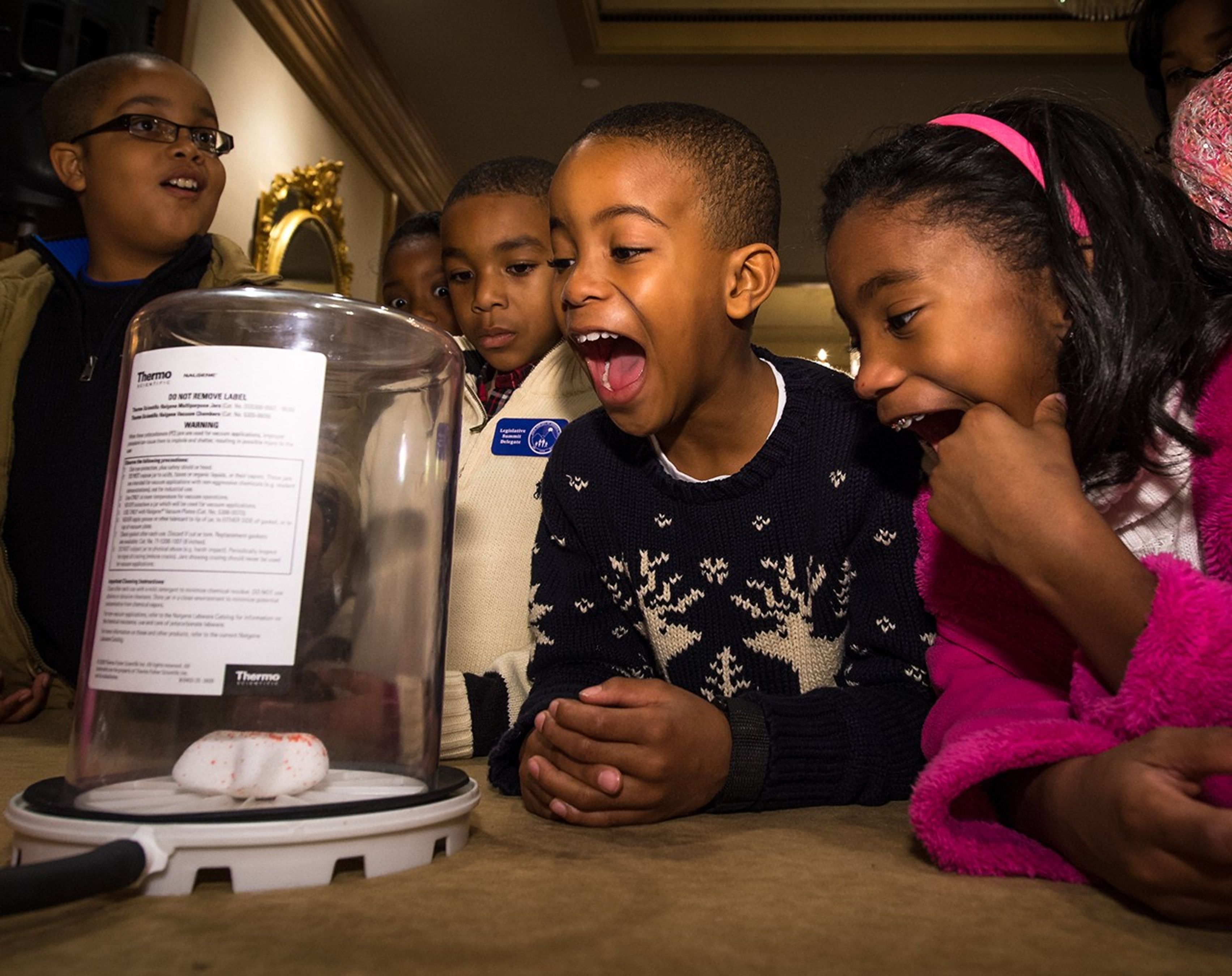 Several students react with joy as they watch a science experiment.