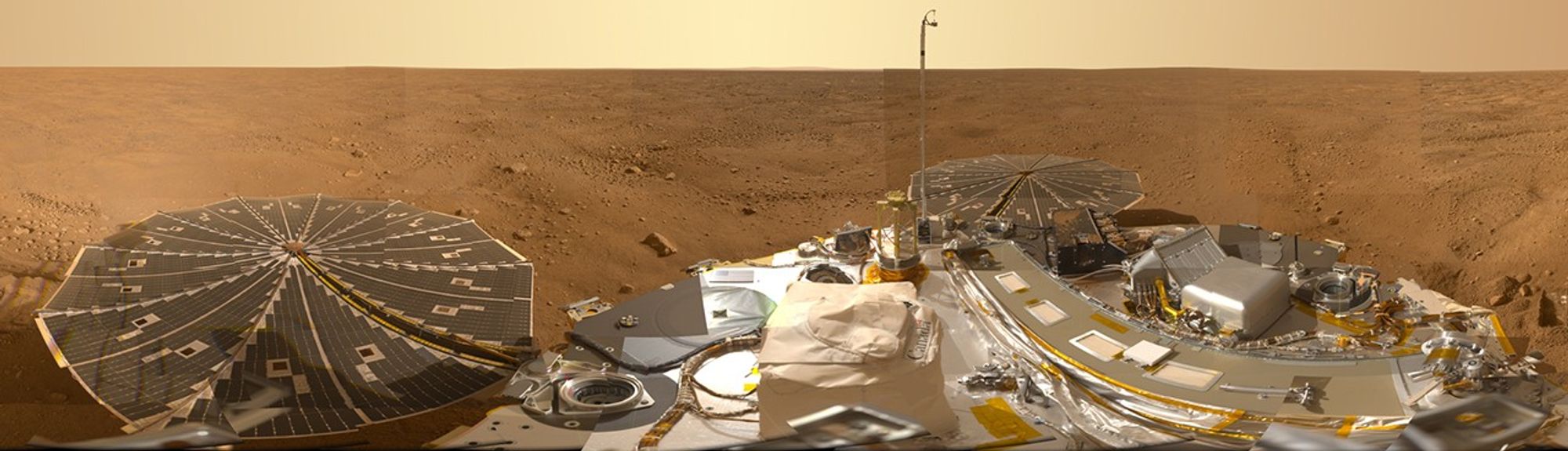 Una vista amplia y plana en la superficie de Marte es visible por encima de los instrumentos y paneles solares del módulo de aterrizaje.