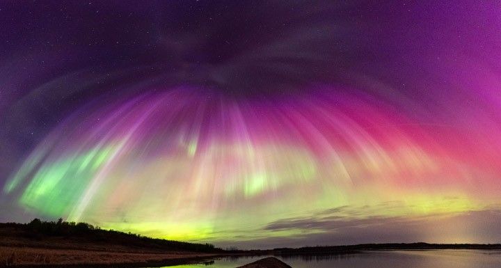 Curtains of brilliantly colorful light appear to curve toward each other in the sky and meet together at the top of the image.