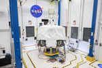 NASA's VIPER robotic Moon rover is shown in a clean room at NASA's Johnson Space Center in Houston. Two of its wheels are visible in this image. It is shown on a white floor in front of a white wall next to the NASA "meatball" logo. On the the floor there is yellow-and-black tape surrounding the rover