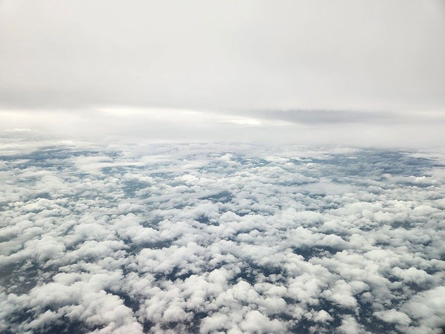 The image shows an aerial view of grey skies above and thick, broken cloud cover below.