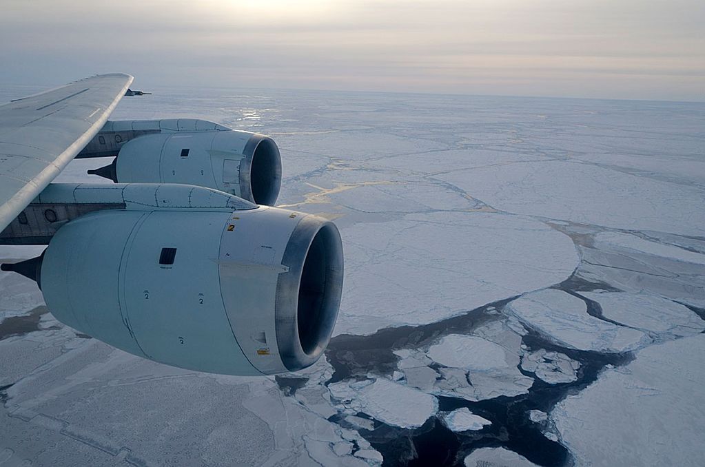Photo of a plane's wing flying over ice in the ocean.