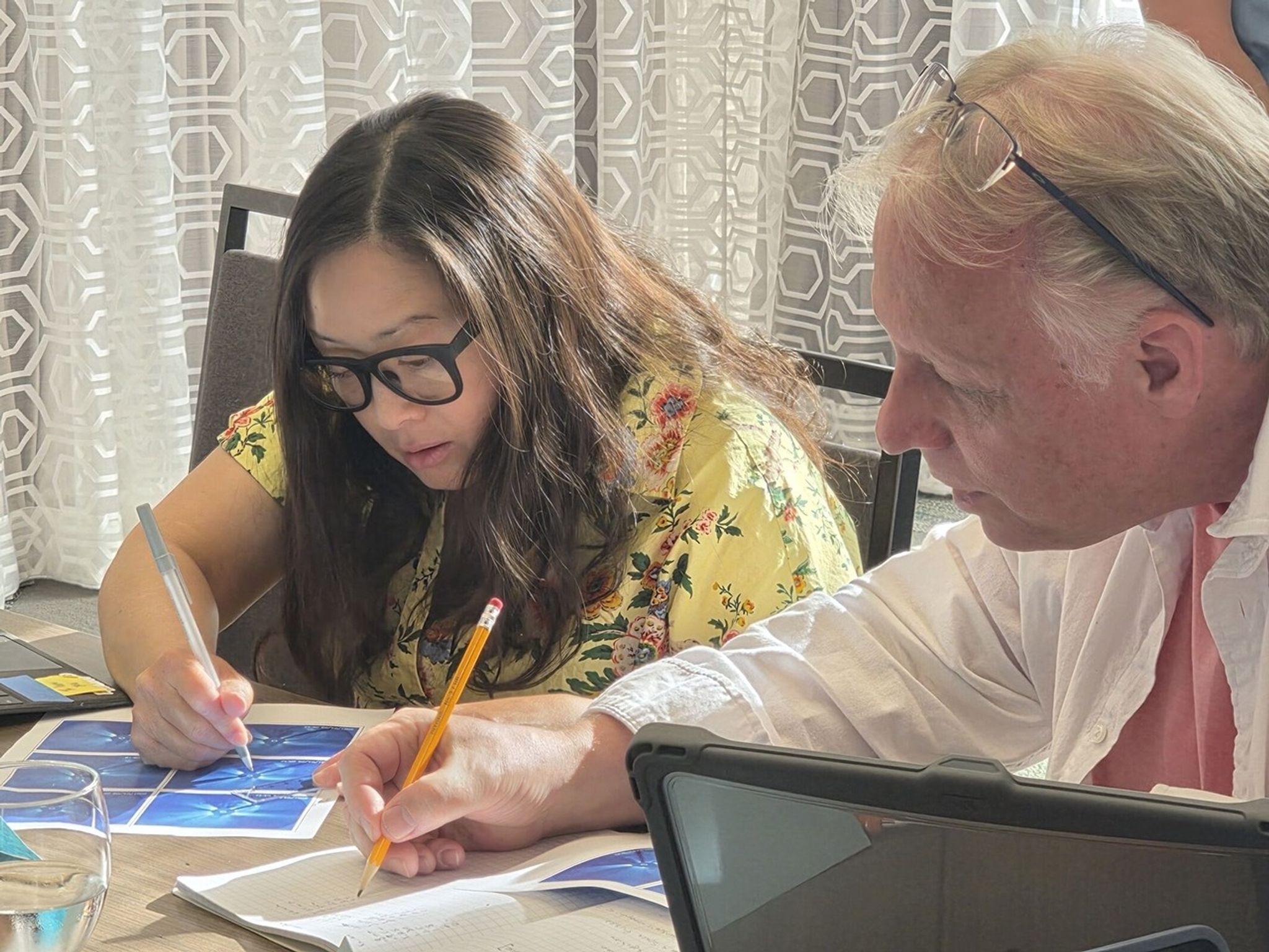 Two teachers look at still images of a coronal mass ejection, using their pencils to note how far the edge of the ejection has moved across the field of view.