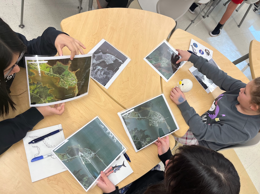 Three students sitting around a classroom table looking at NASA satellite images.