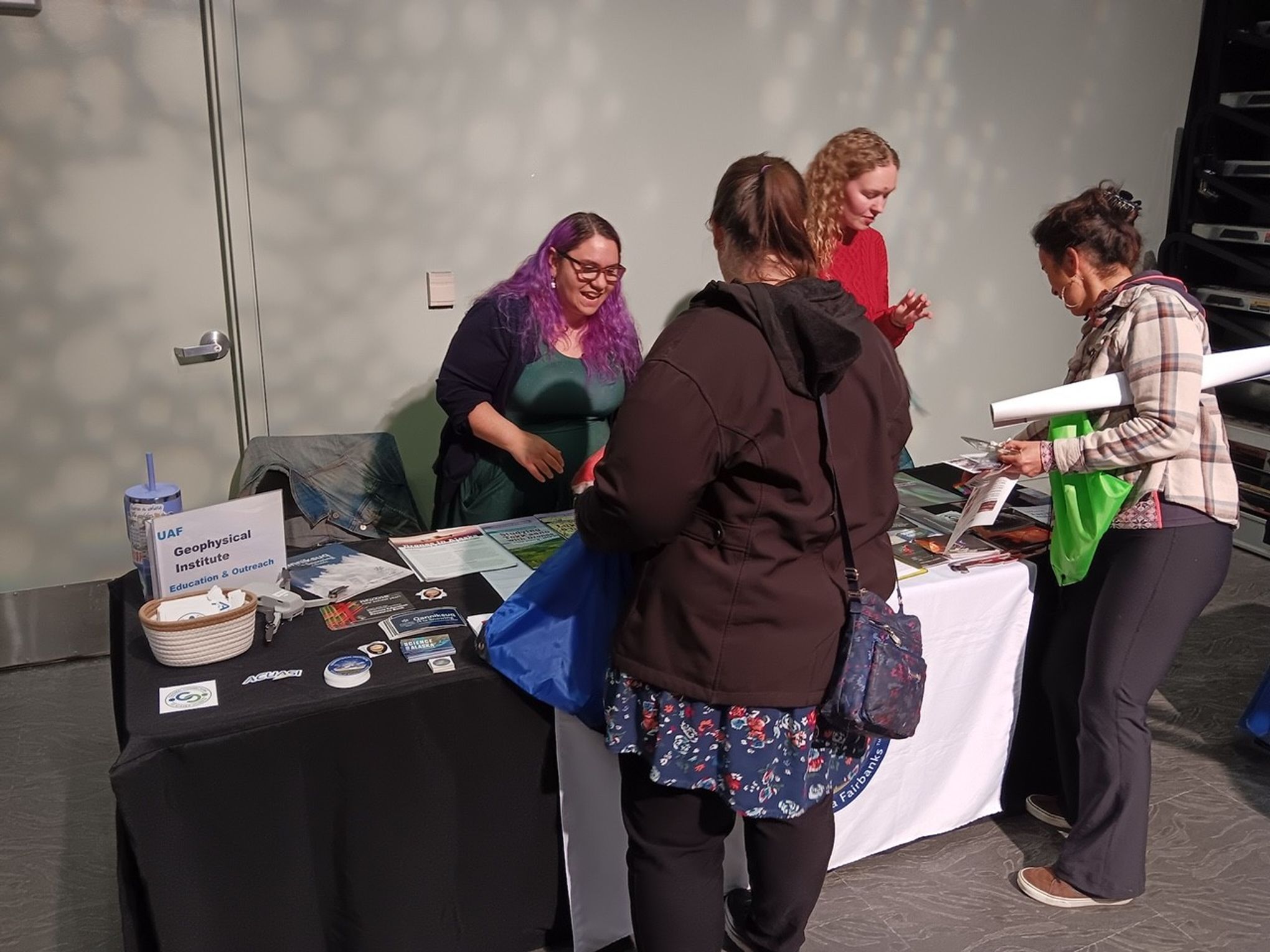 Two visitors are interacting with two women (staff), looking at some materials on a table.