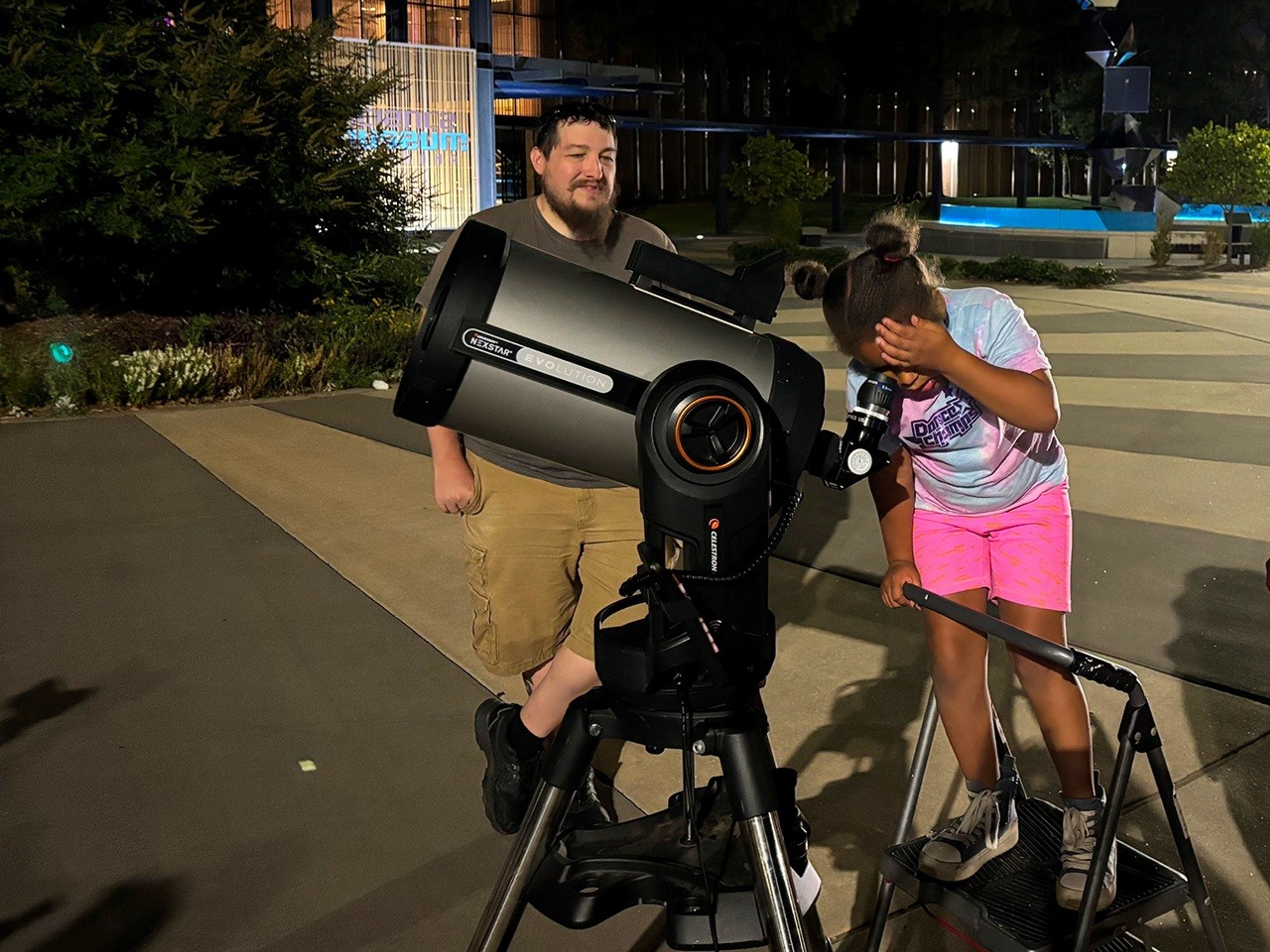 A child looking through a telescope with the help of an amateur astronomer.