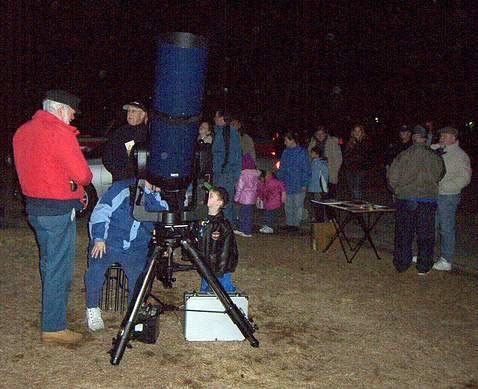 A group of people at a star party, looking through a large blue telescope.