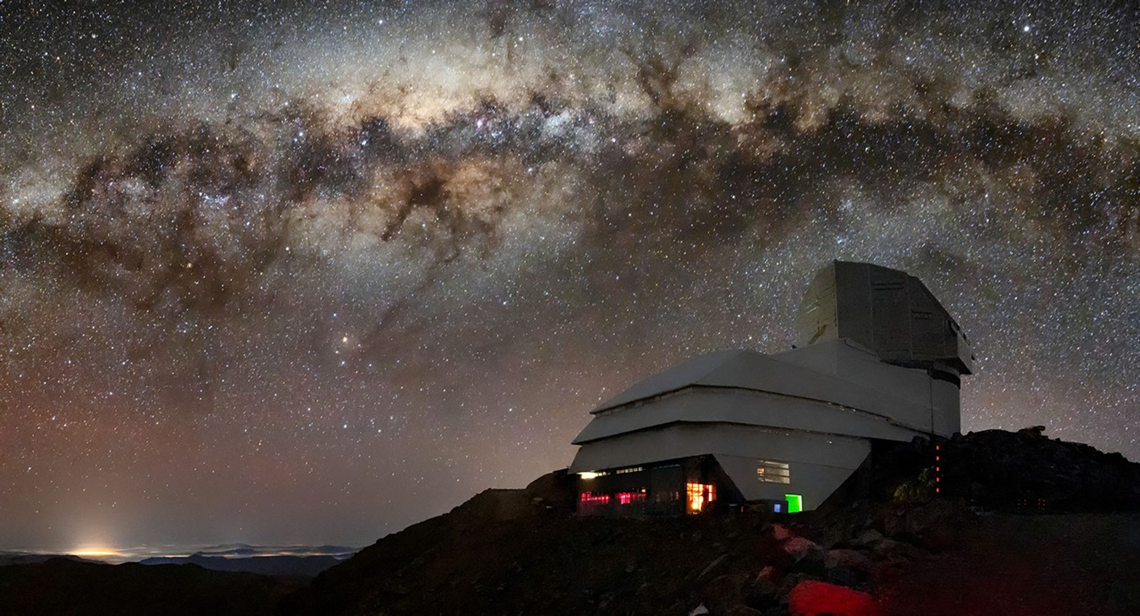 This image captures not only Vera C. Rubin Observatory, a Program of NSF NOIRLab, but one of the celestial specimens Rubin Observatory will observe when it comes online: the Milky Way. The bright halo of gas and stars on the left side of the image highlights the very center of the Milky Way galaxy. The dark path that cuts through this center is known as the Great Rift, because it gives the appearance that the Milky Way has been split in half, right through its center and along its radial arms. In fact, the Great Rift is caused by a shroud of dust, which blocks and scatters visible light.