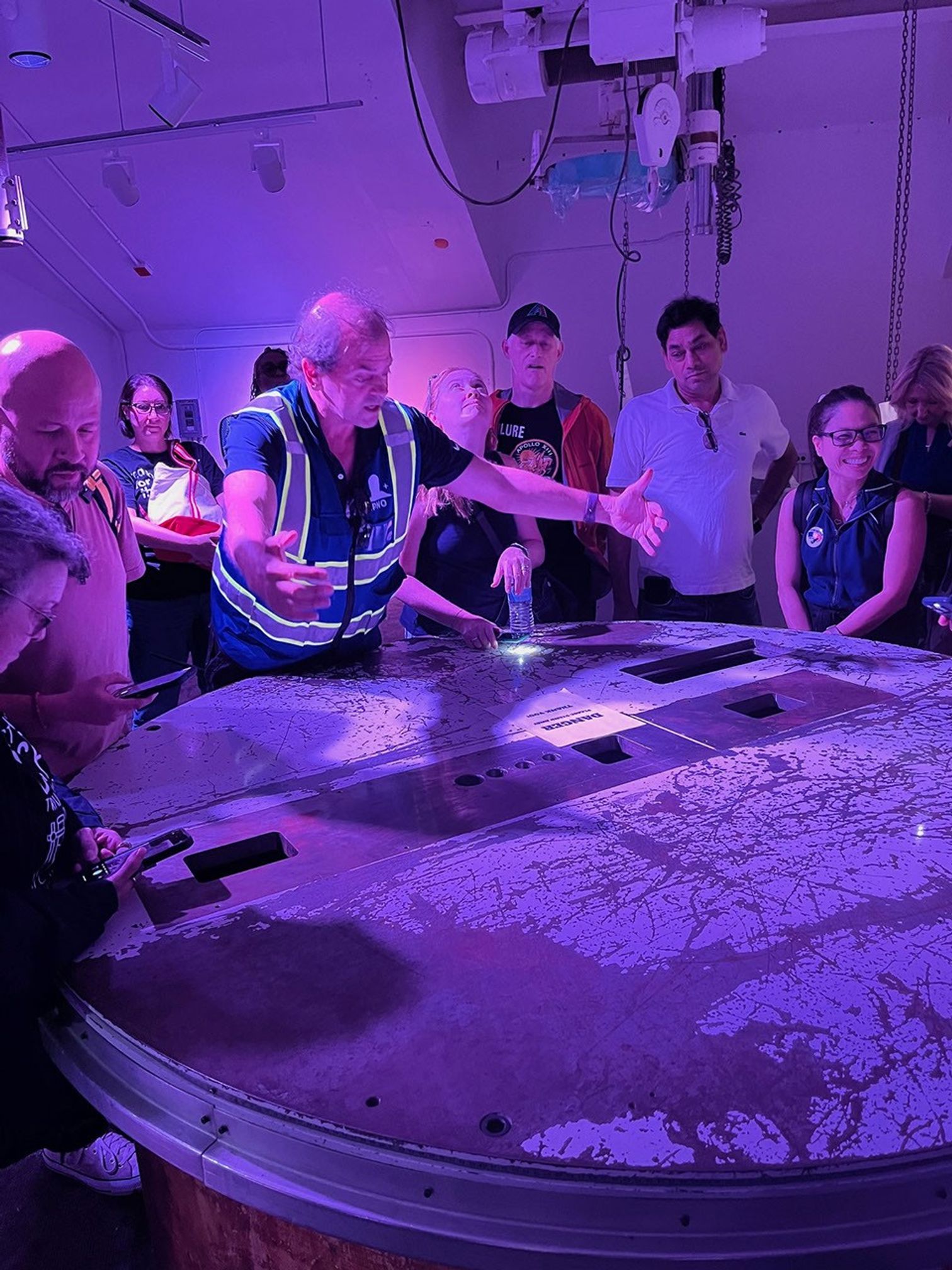 Group of people, one gesturing with arms spread, gathered around a wide circular table.