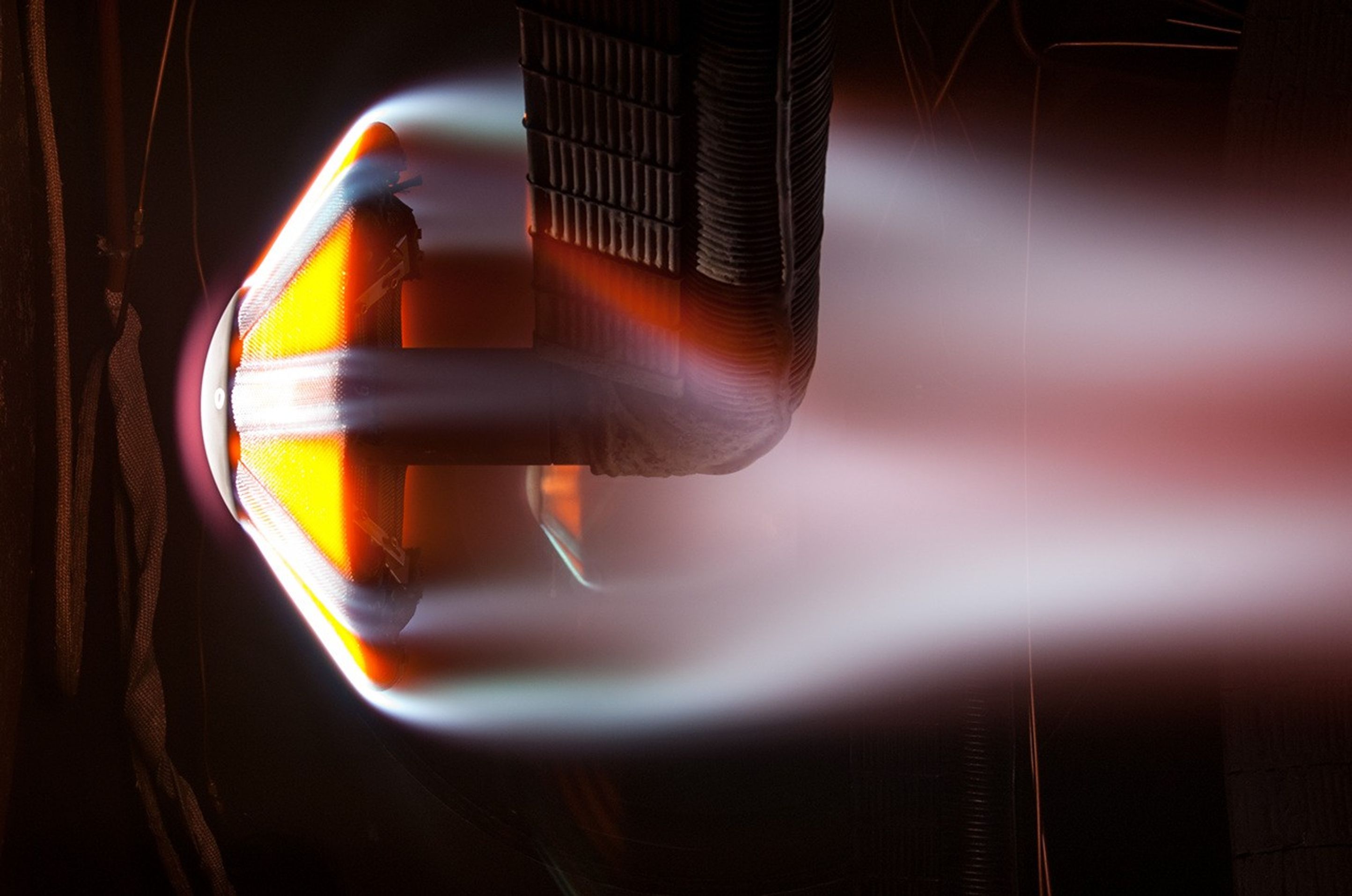 Close-up image of a heat shield during a high-temperature test, with bright orange glow and aerodynamic flow lines simulating reentry conditions.