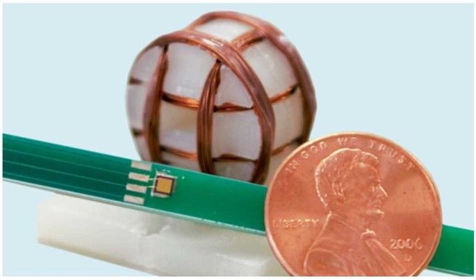 Small electronic sensor next to a penny for scale, with a spherical object wrapped in copper wire in the background.