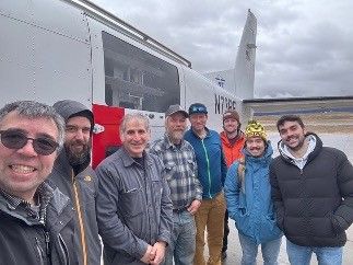 A group of people in winter clothes standing beside a mid-sized airplane.