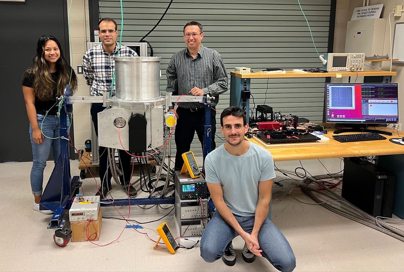 Three team members surrounding a metal dewar with optics and a computer screen displaying an image from the sensor.