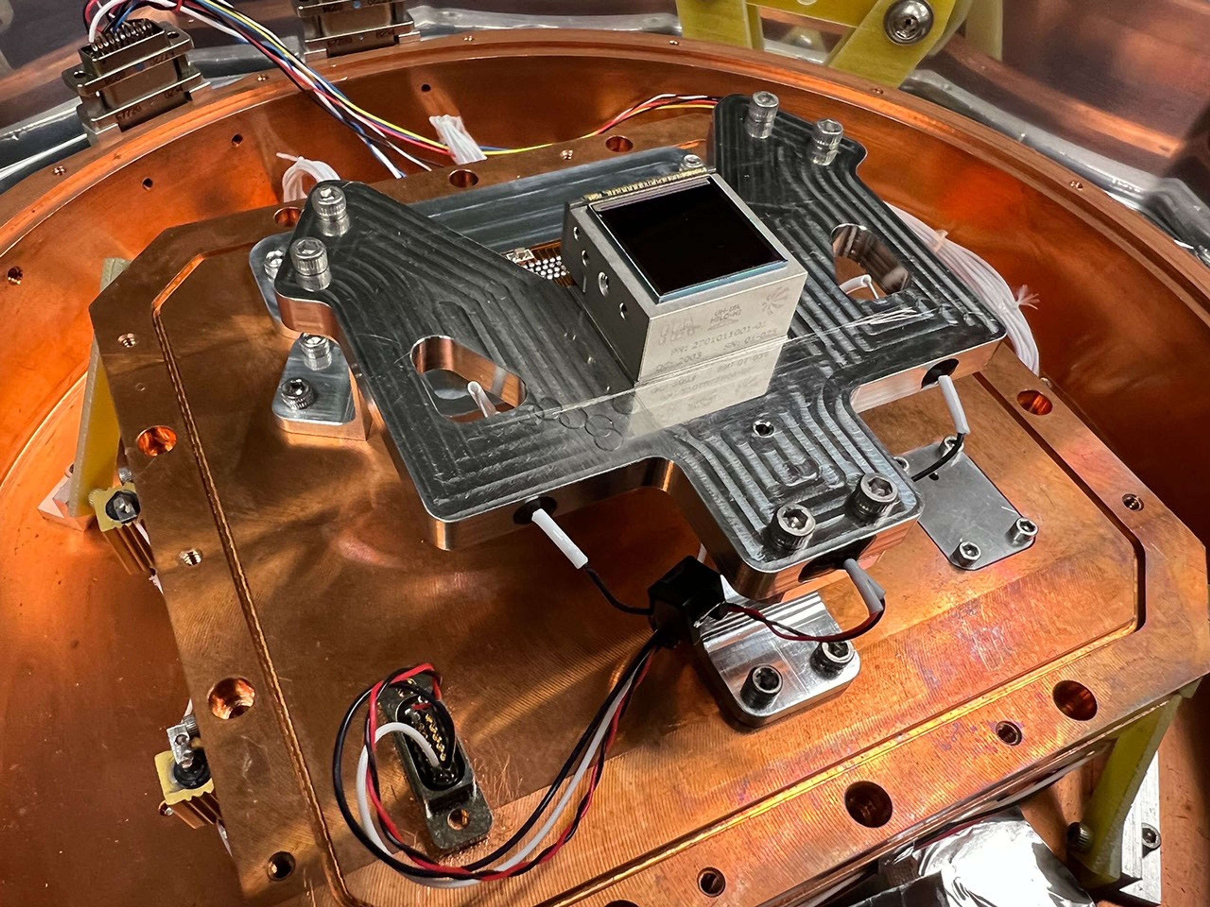 Three team members surrounding a metal dewar with optics and a computer screen displaying an image from the sensor.