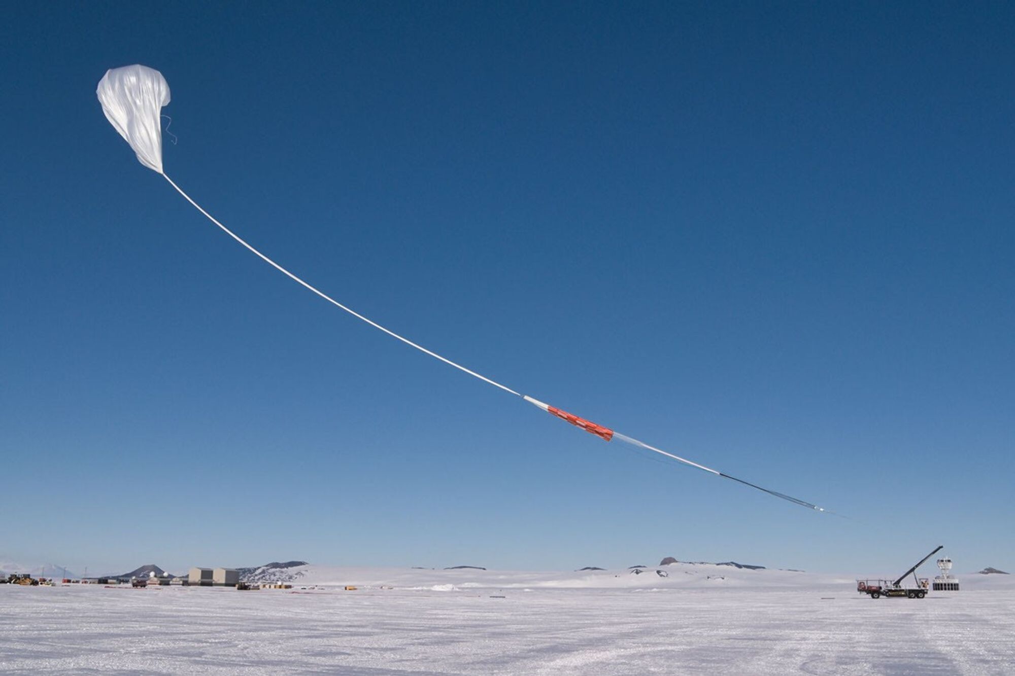 A white balloon with a long tether hovering above the icy ground