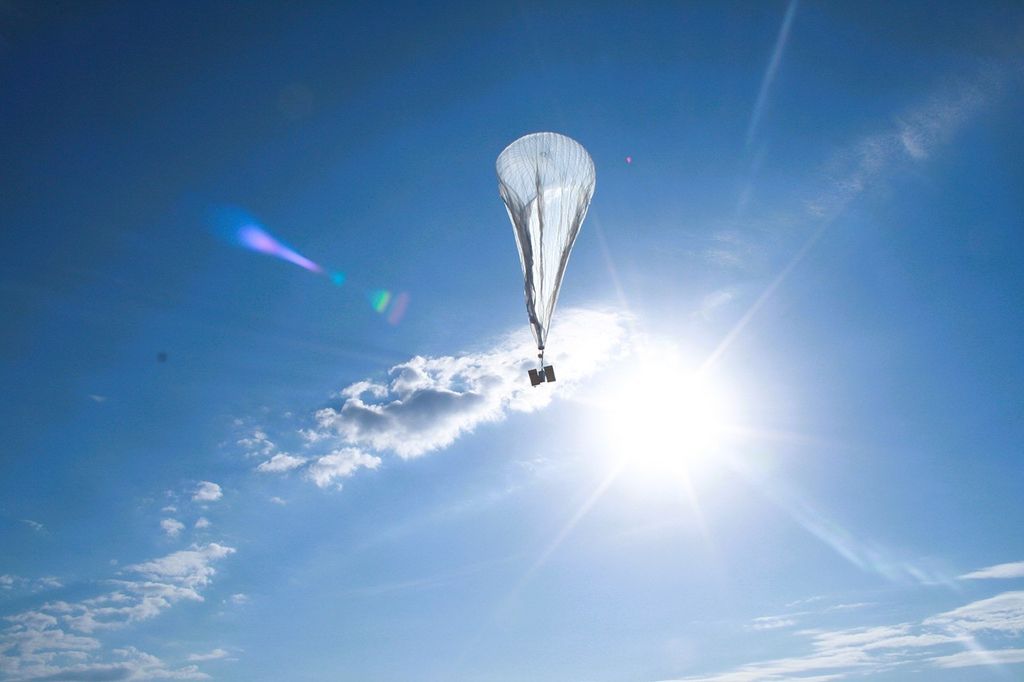 A partially inflated scientific balloon rises in to a blue, partly cloudy sky.