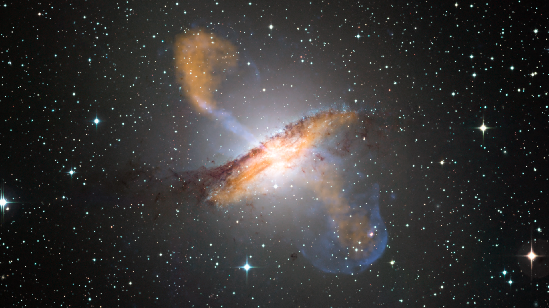 This composite of visible, microwave (orange) and X-ray (blue) data reveals the jets and radio-emitting lobes emanating from Centaurus A's central black hole. Credit: ESO/WFI (visible); MPIfR/ESO/APEX/A.Weiss et al. (microwave); NASA/CXC/CfA/R.Kraft et al. (X-ray)