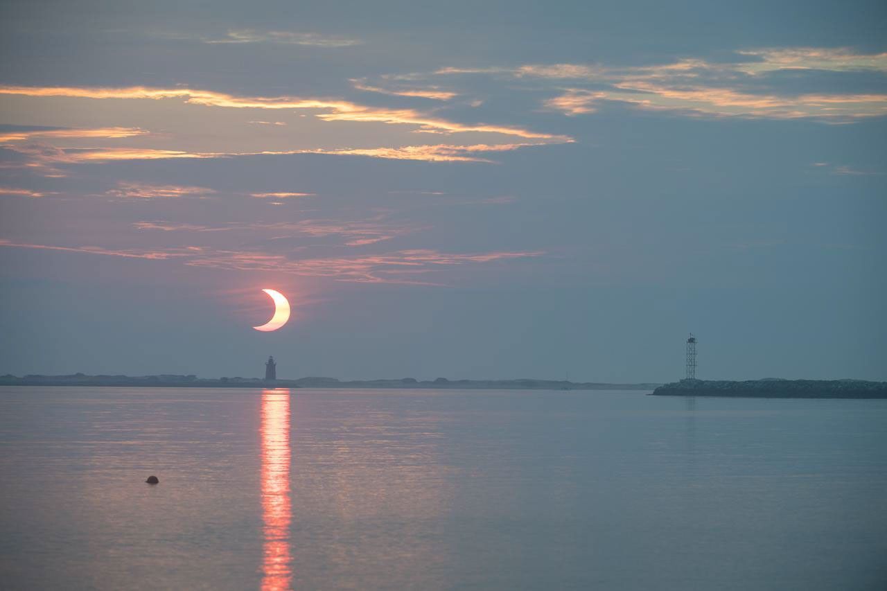 A partial solar eclipse is seen as the sun rises behind the Delaware Breakwater Lighthouse, Thursday, June 10, 2021, at Lewes Beach in Delaware. The annular or “ring of fire” solar eclipse is only visible to some parts of Greenland, Northern Russia, and Canada. Photo Credit: (NASA/Aubrey Gemignani)