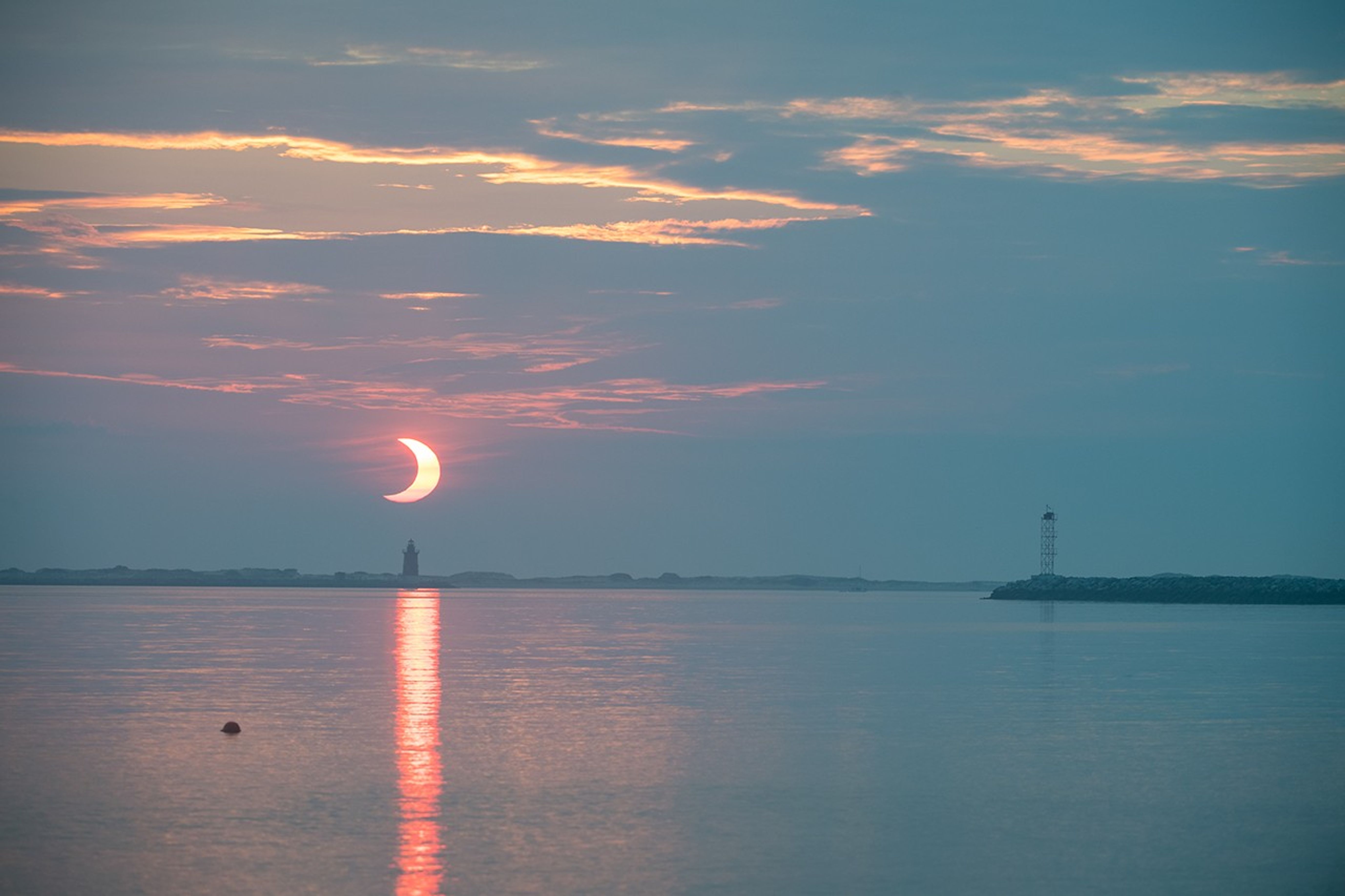 A partial solar eclipse is seen as the sun rises behind the Delaware Breakwater Lighthouse, Thursday, June 10, 2021, at Lewes Beach in Delaware. The annular or “ring of fire” solar eclipse is only visible to some parts of Greenland, Northern Russia, and Canada. Photo Credit: (NASA/Aubrey Gemignani)