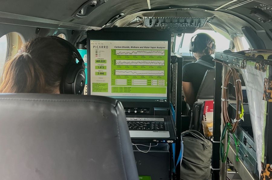 A computer screen displays live readings of carbon dioxide, methane, and water vapor concentrations. Scientists monitor readings from inside the Gulfstream’s small cabin.