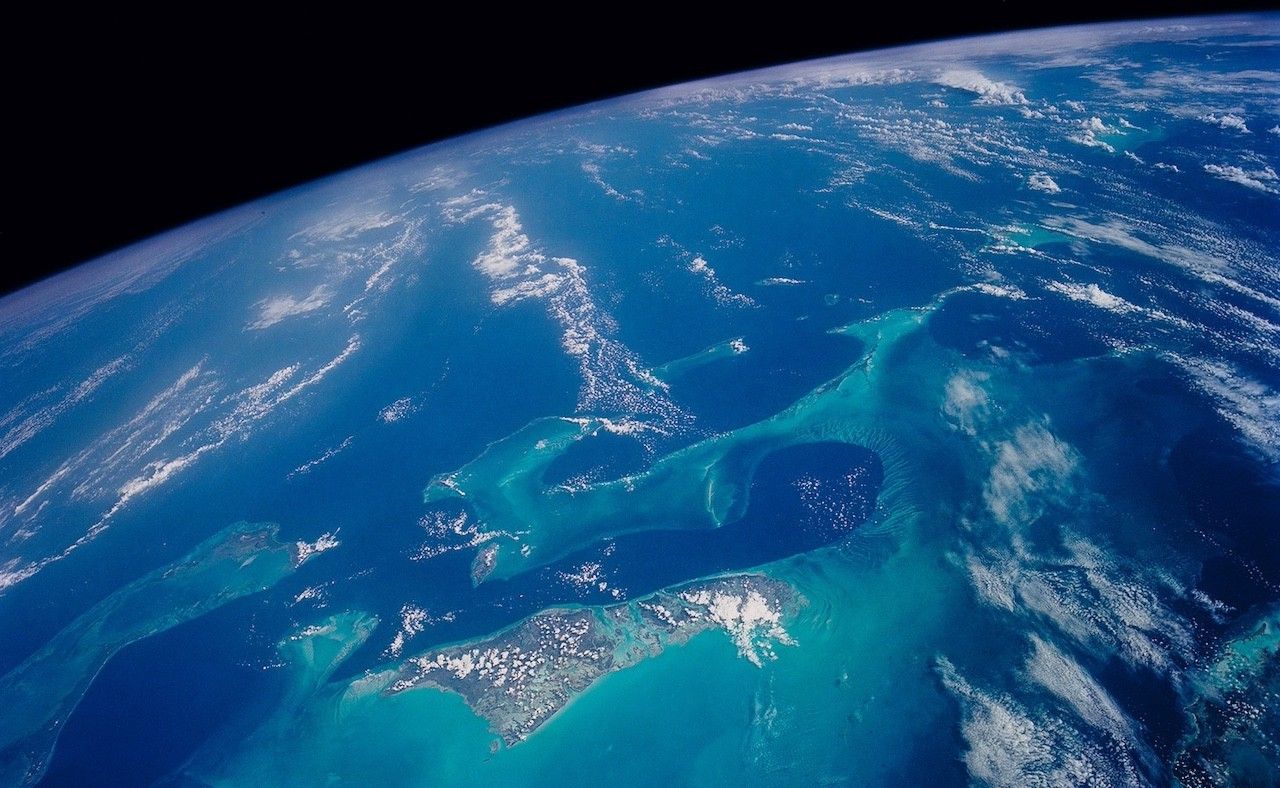 Satellite image of the Bahamas that includes the dark of space in the top left. The bright blue waters of the Bahamas apparent in the foreground.