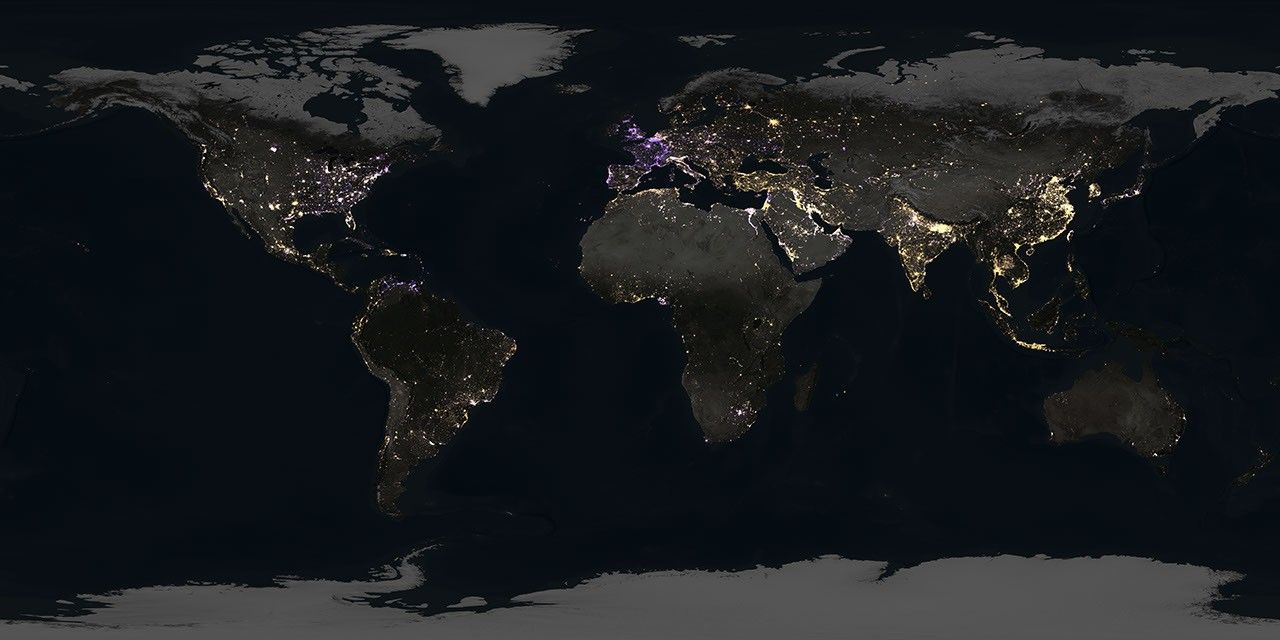 Gold, purple, and white points of light brighten up a globe shrouded in darkness, while a shaft of sunlight is just visible peeking over the edge of the planet.