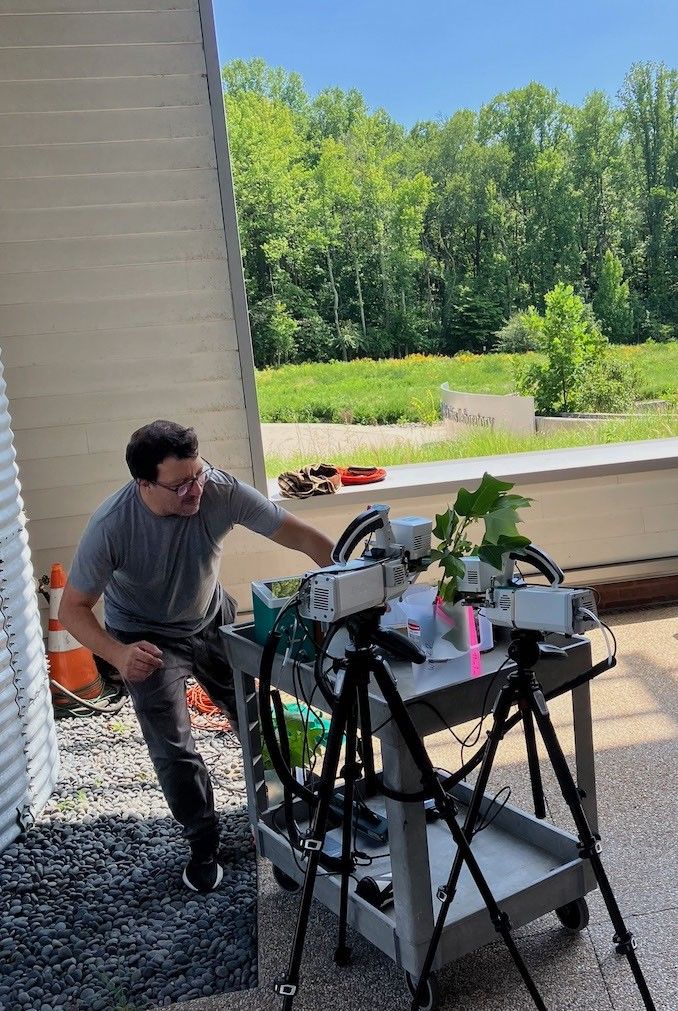 In a sheltered open air passageway, a man works with instruments and leaves on a lab cart.