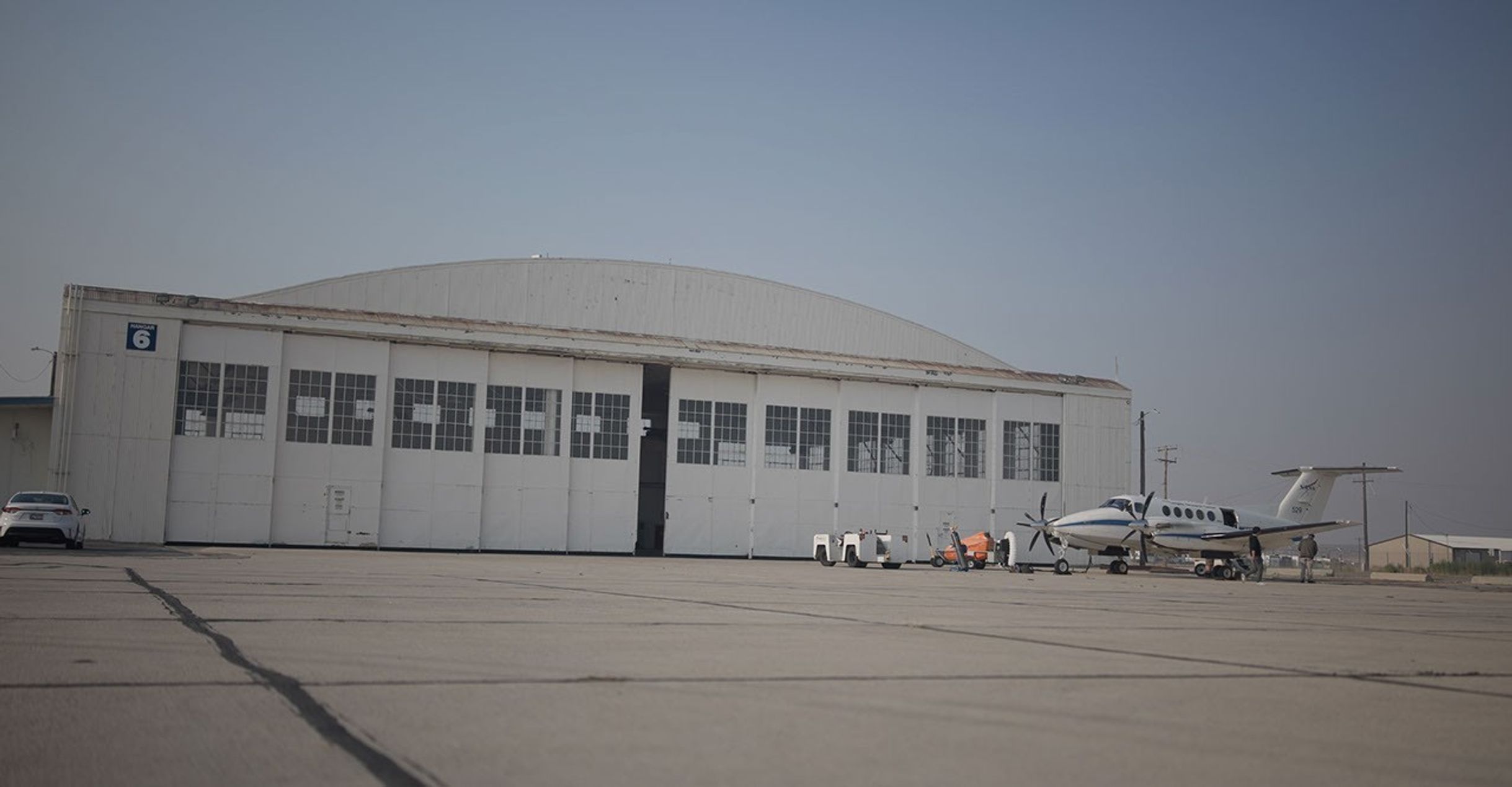 A large metal aircraft hangar behind a twin-propeller NASA airplane.