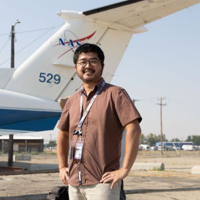 A smiling man stands beside a mid-sized NASA aircraft