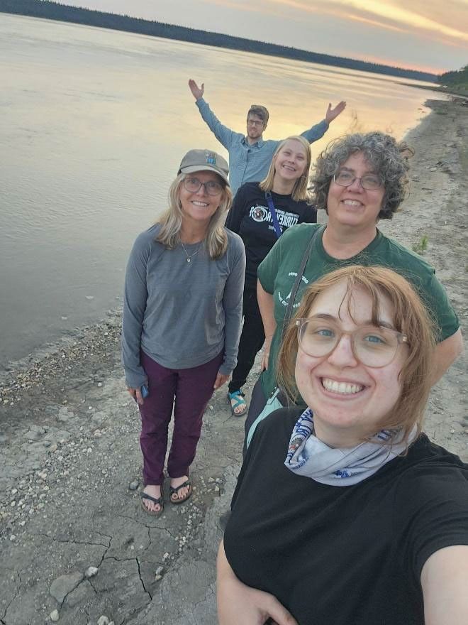 A selfie of the group of five researchers, smiling at the edge of a gray lake reflecting the sunset. They’re wearing sandals; they look radiant. In the background, Cook throws both arms wide, a triumphant gesture.
