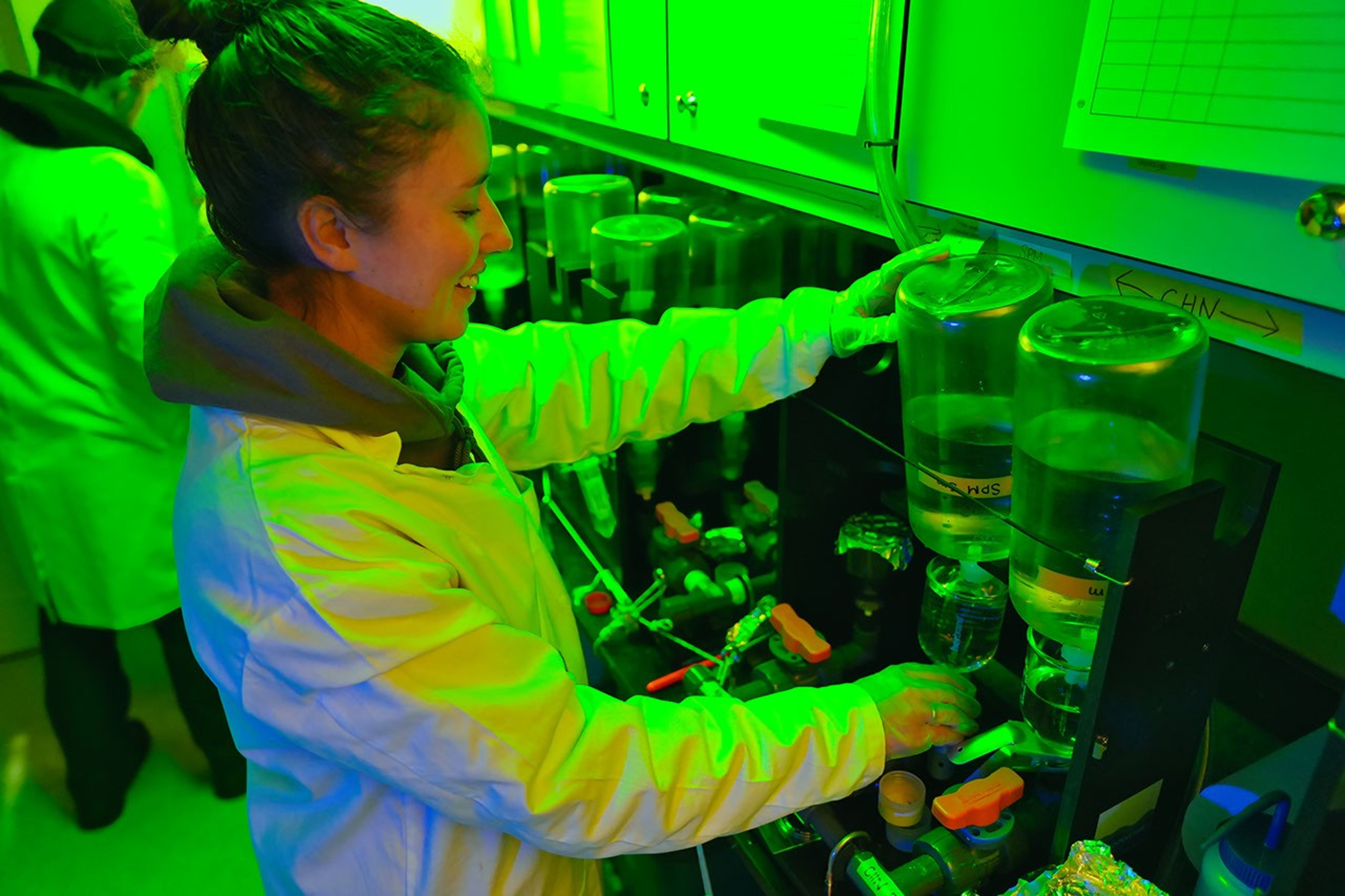 Glowing with neon green light, a woman works with a water filtration system in a lab inside the ship.