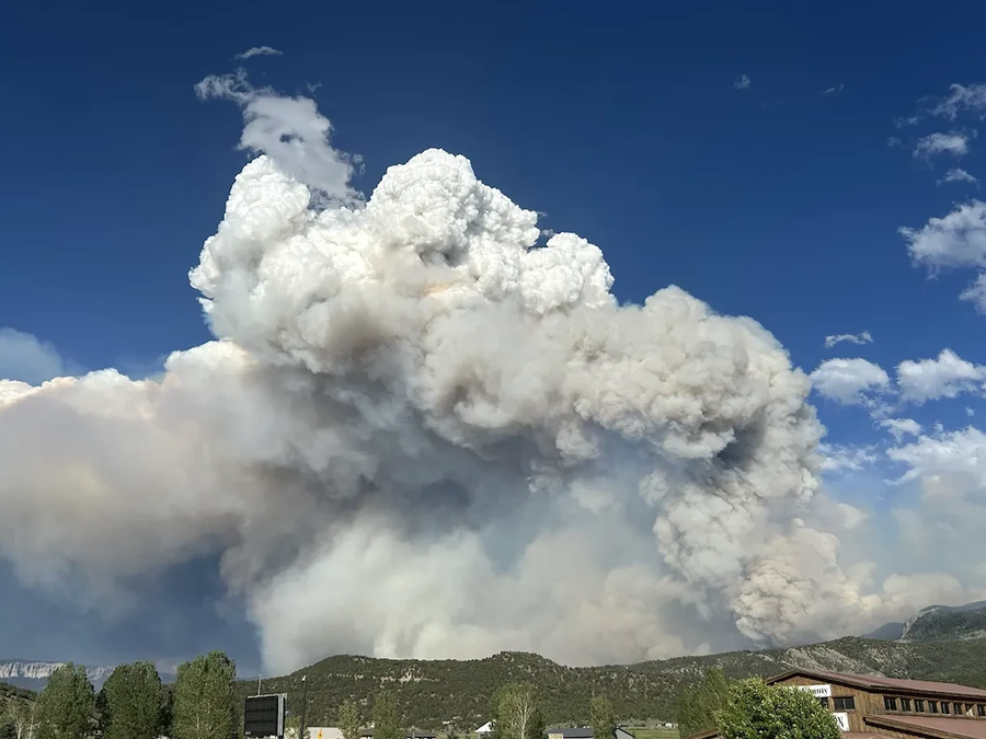 A towering, smoky cloud looms over green mountains.