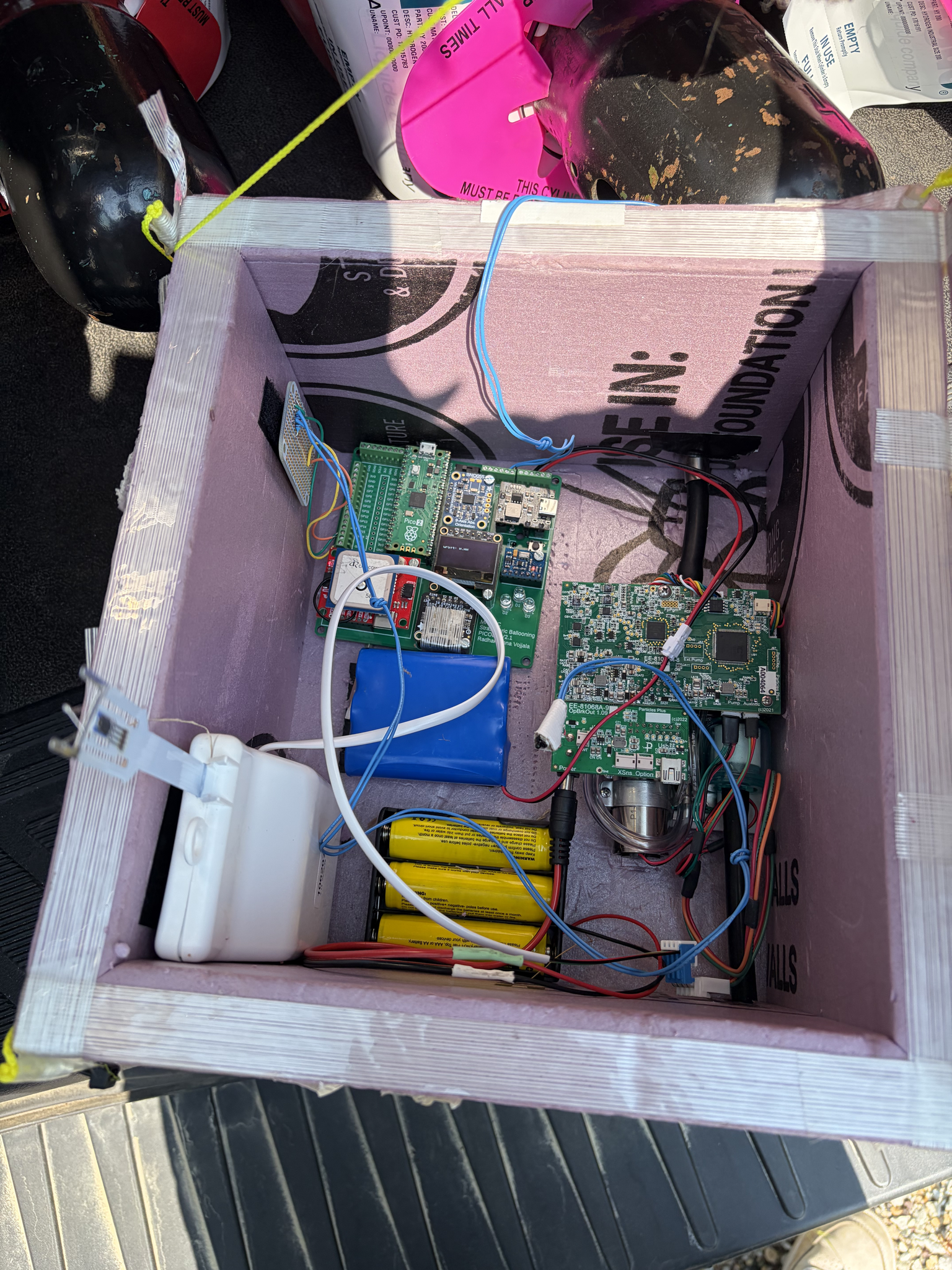 A mauve box with white edges contains computer components, battery packs, and wires.