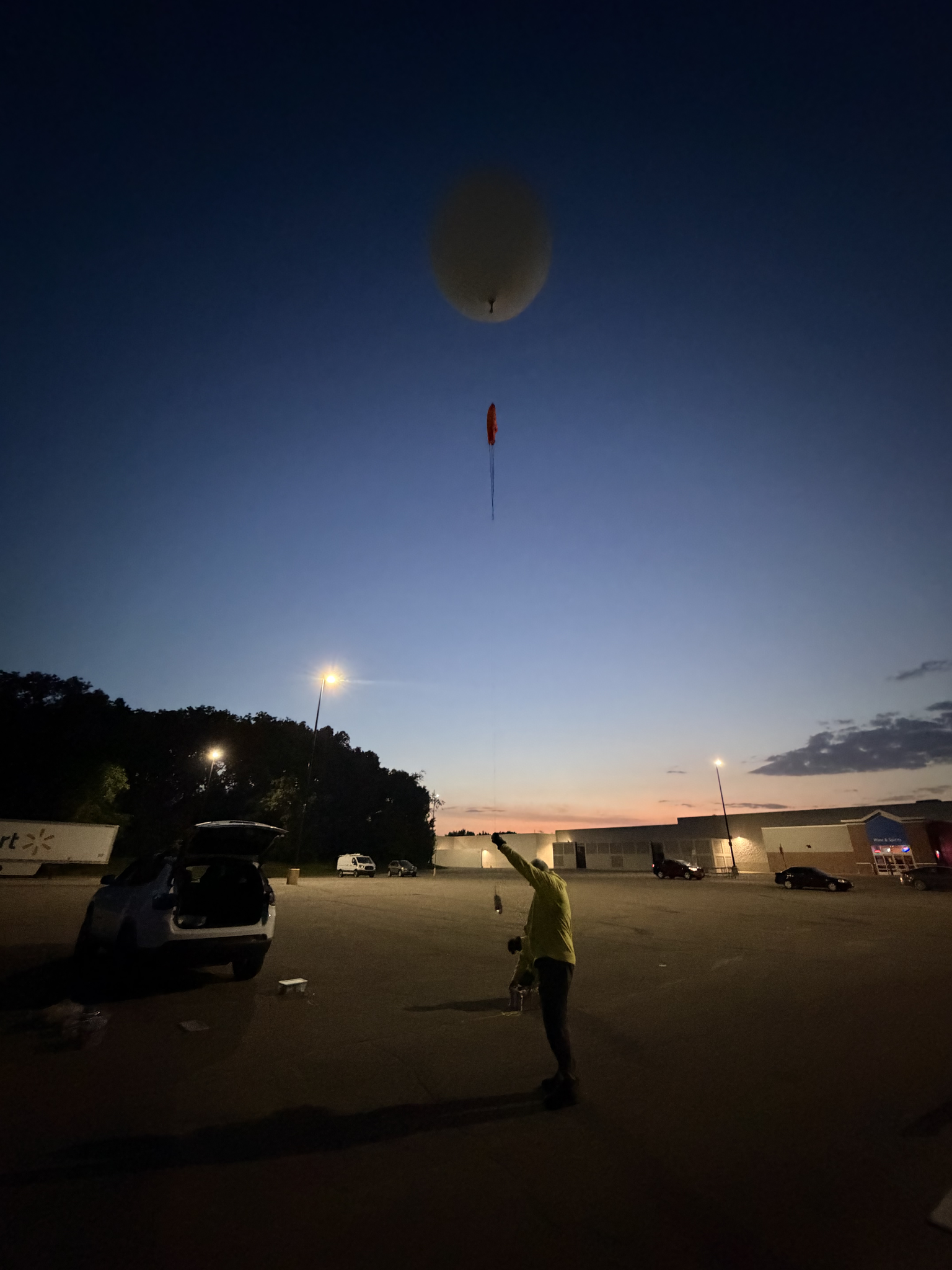 A weather balloon, lit gray in the dawn light, rises above its launch position.