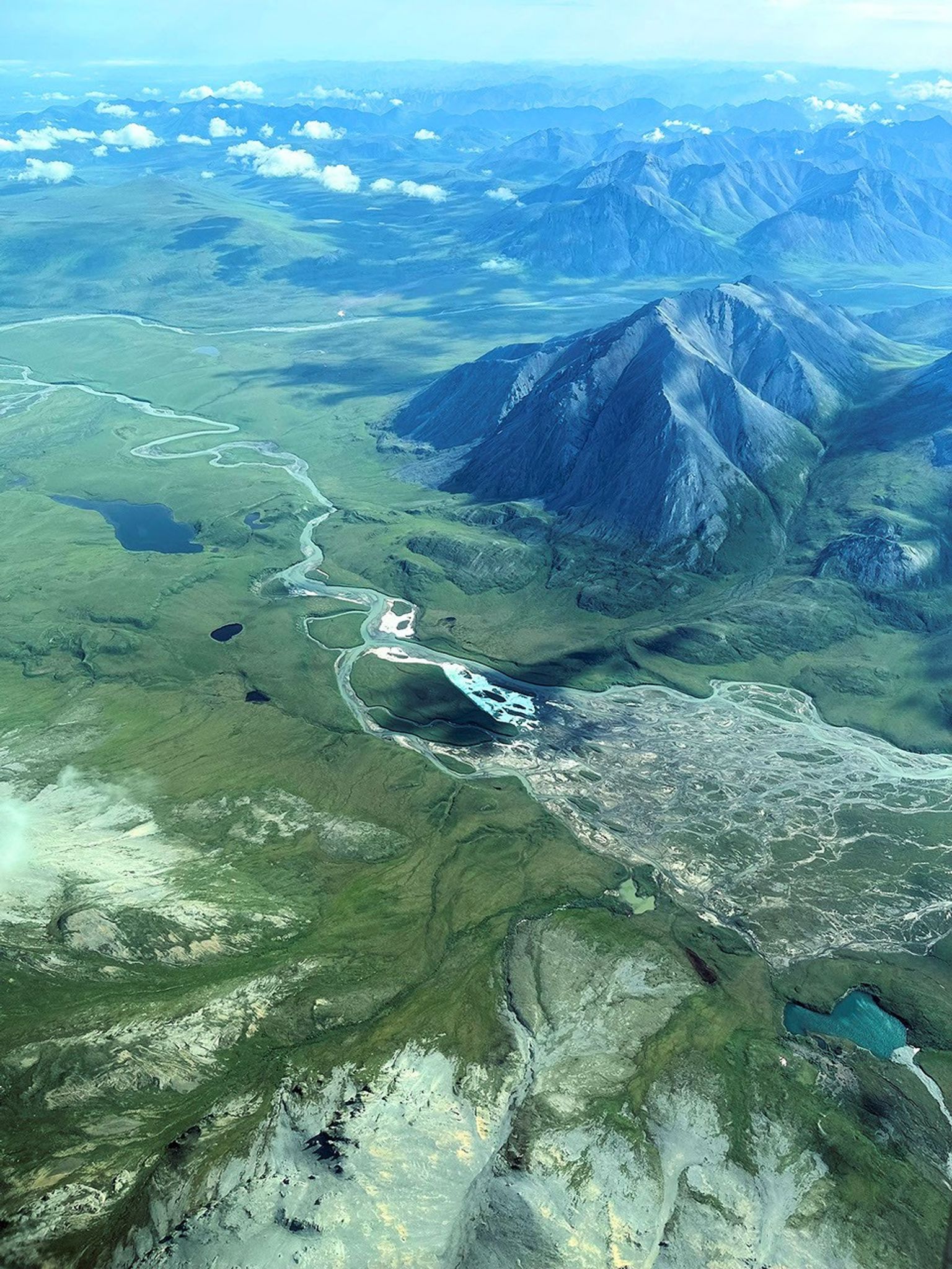 Sharp blue mountain peaks spring up alongside rolling green hills. Pale blue rivers wind from the mountains through the low-lying areas.