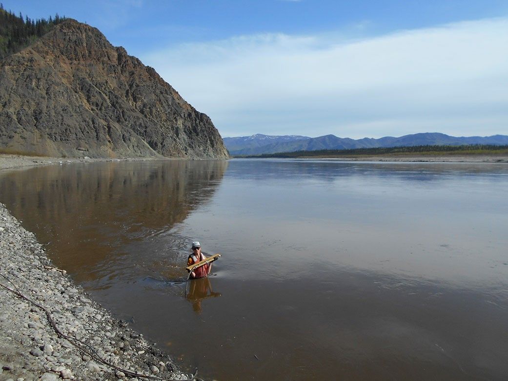 Photo of a scientist making measurements while waste-deep in a stream
