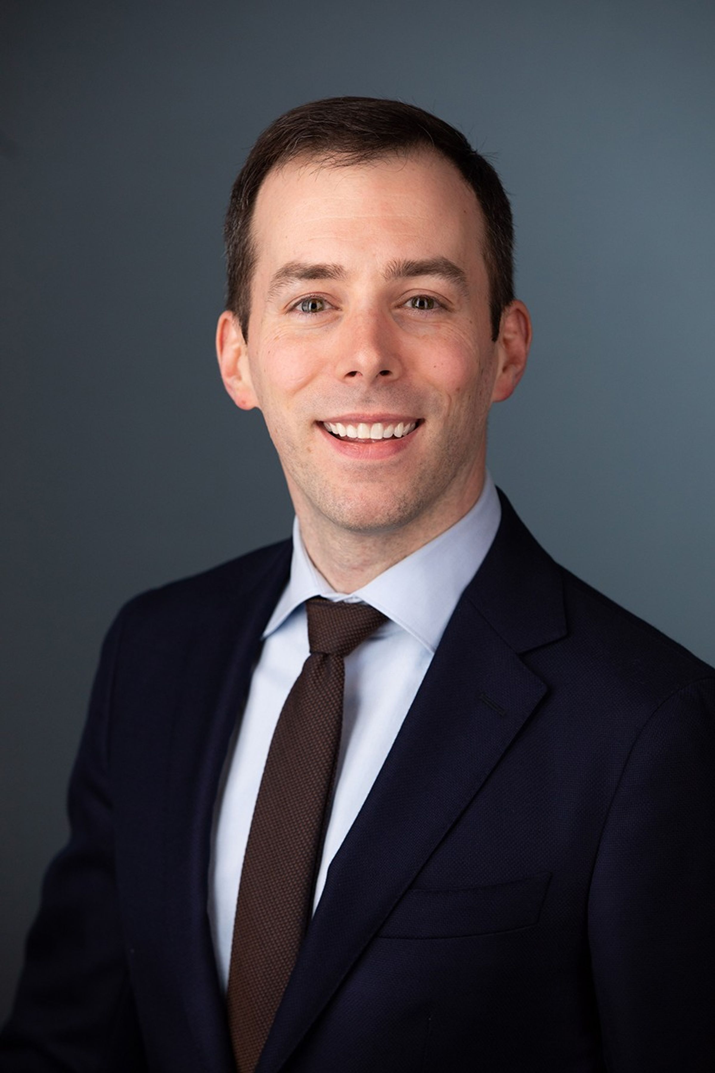 Photo of a smiling Justin Stachnik in a suit jacket and tie