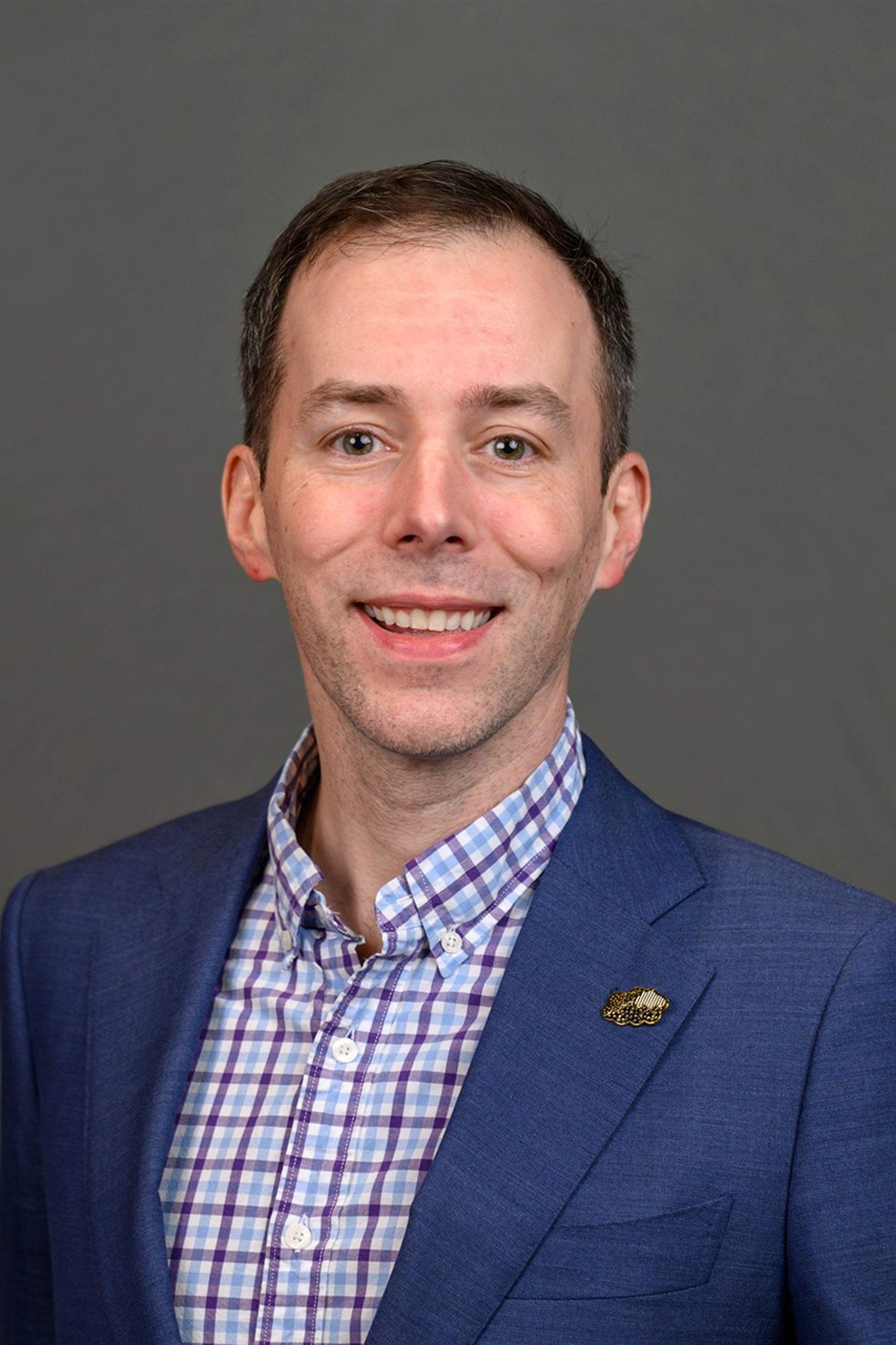 Photo of a smiling Justin Stachnik in a suit jacket and tie
