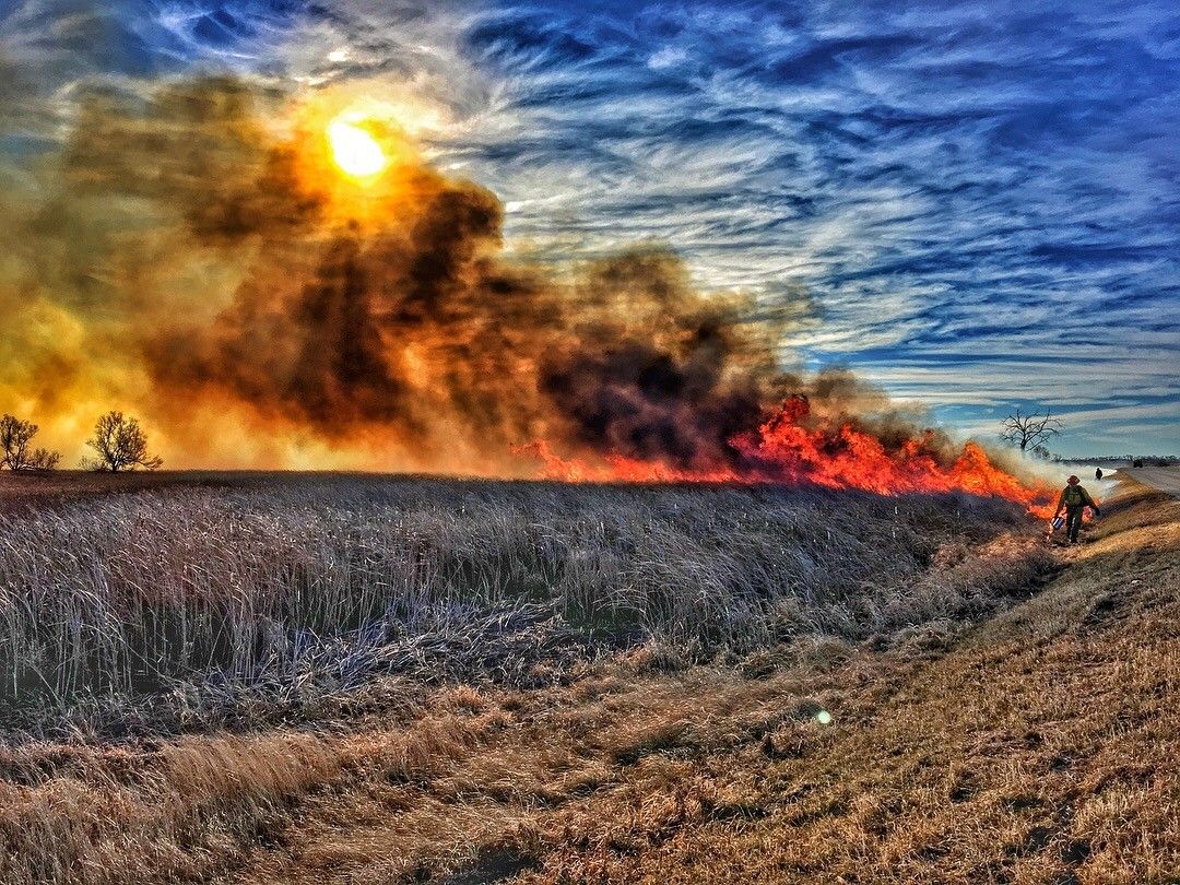 Image of fire in the lower right along the roadside with smoke billowing up and left partially obscuring the sun