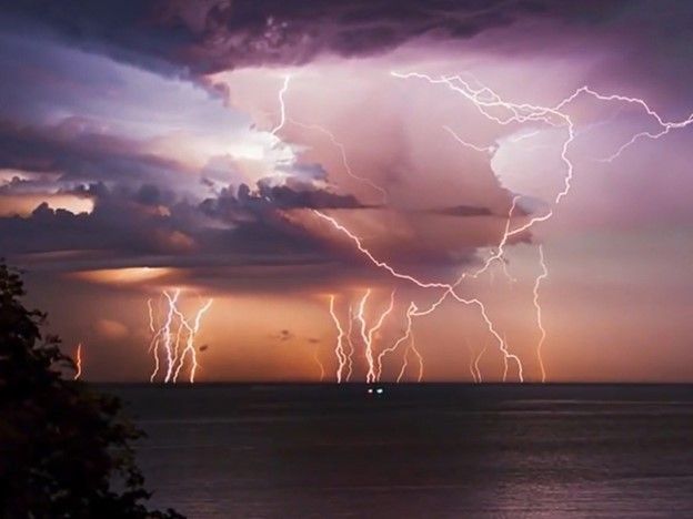 Multiple lightning strikes span the stretch from open waters to peach and somewhat purple color skies. color