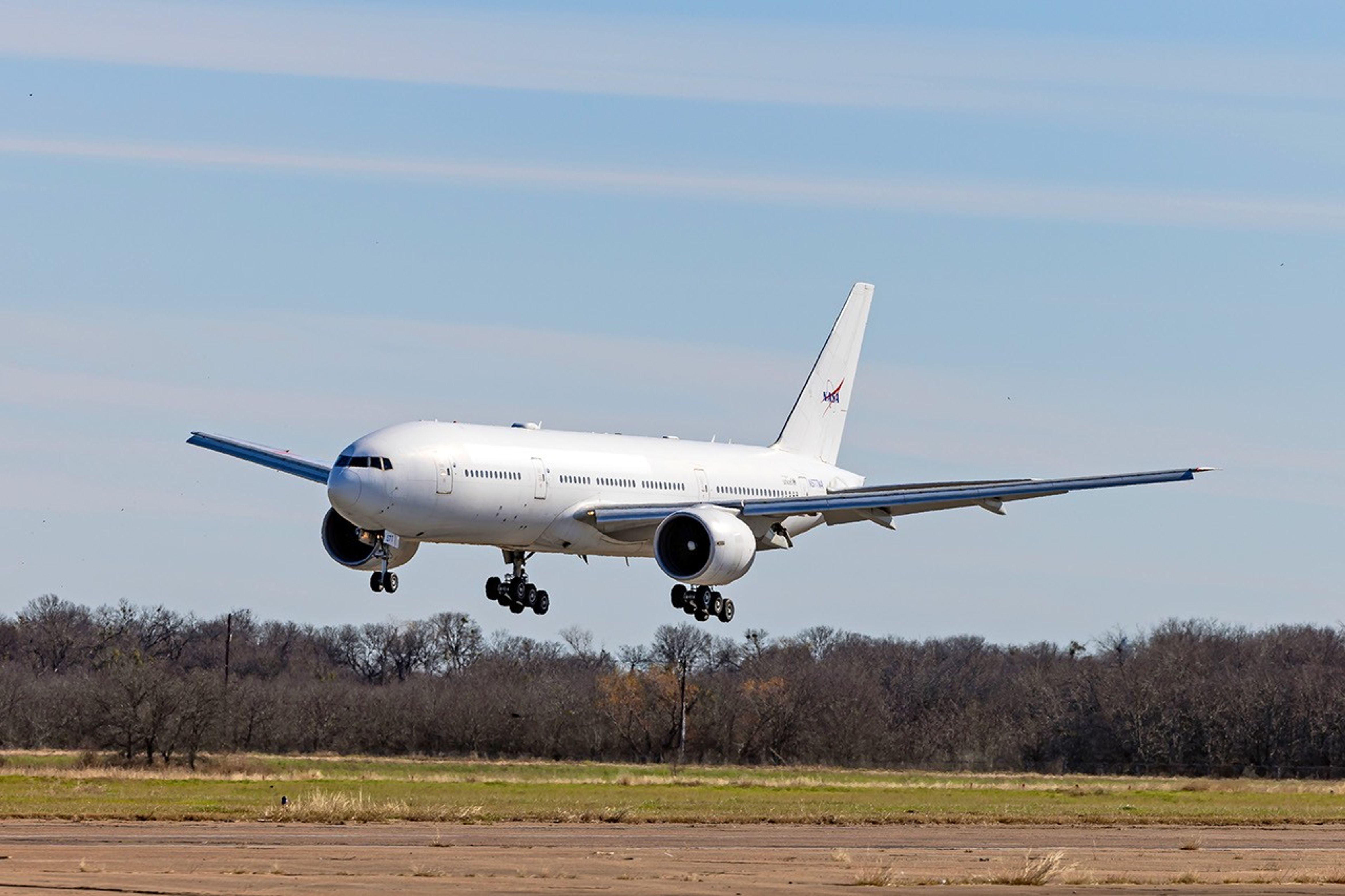 A large white aircraft with a NASA logo on the tail prepares to land on a runway.