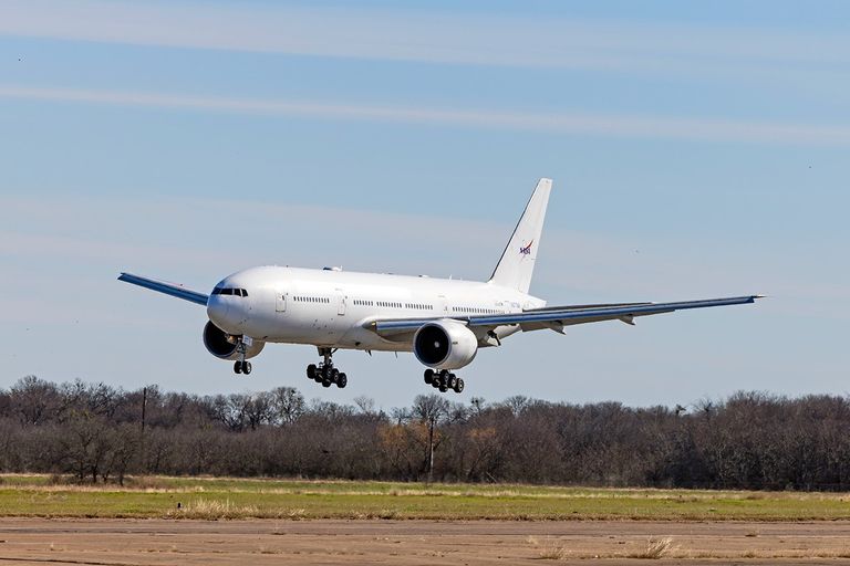 A large white aircraft with a NASA logo on the tail prepares to land on a runway.