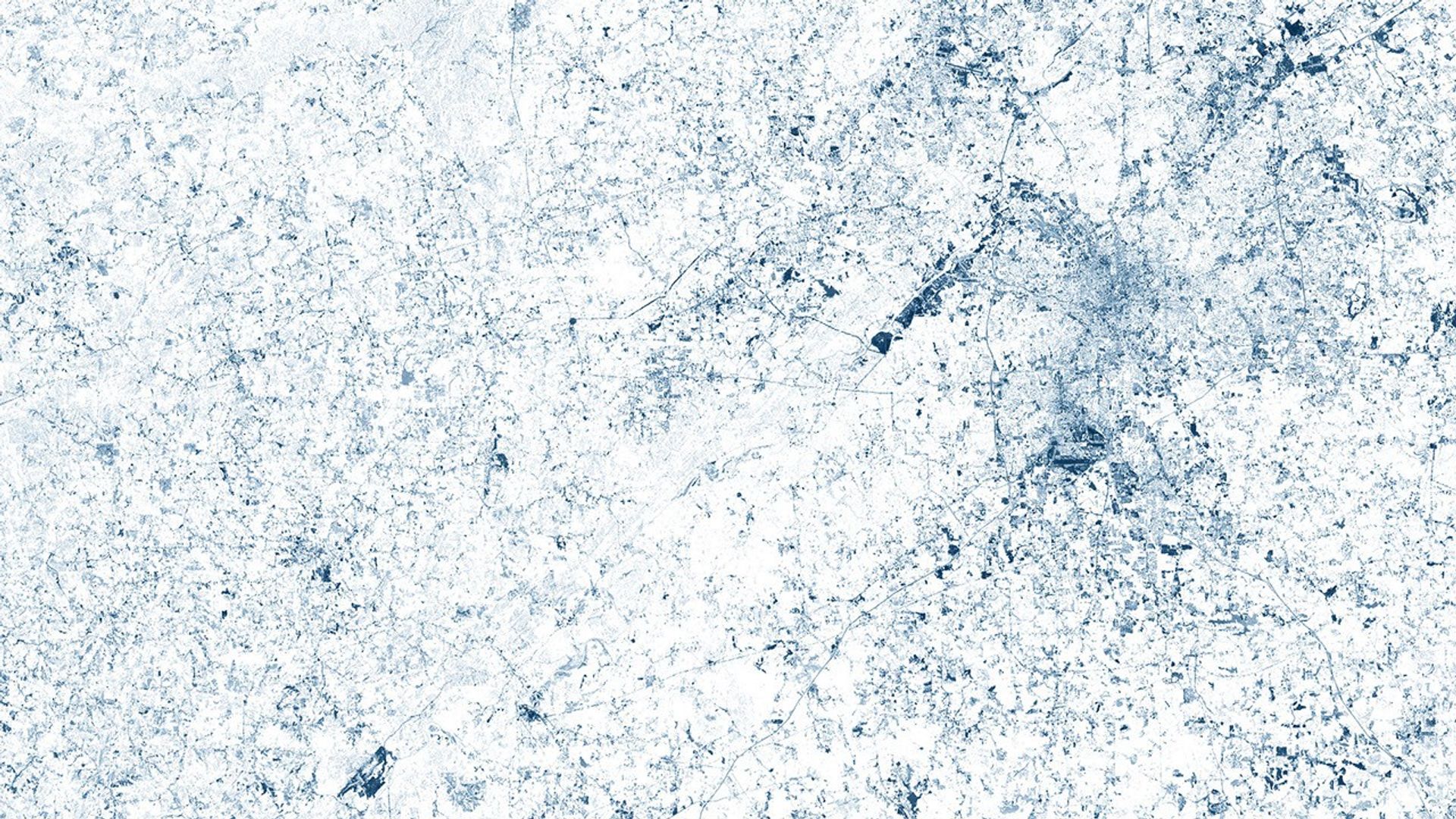 A false-color satellite image of Atlanta's metropolitan area showing urban development as dark blue patterns against a white background representing forested areas. The image was created using green wavelength measurements from Landsat satellite data to emphasize the contrast between developed and rural regions.