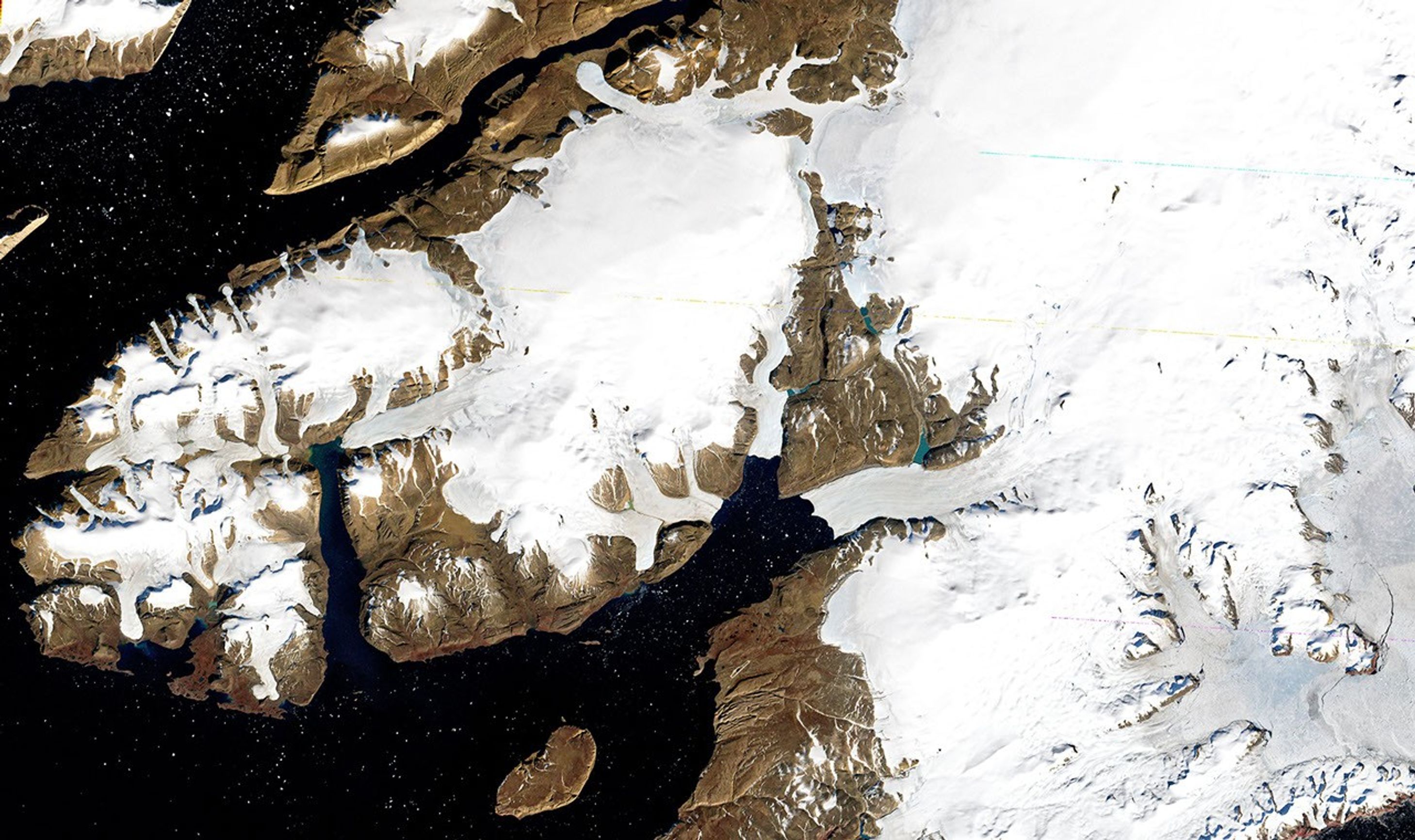 A satellite image of northwest Greenland showing a peninsula north of Thule Air Base. The image captures the North Ice Cap, Wolstenholme Fjord, and surrounding glaciers. White ice and snow cover contrast with brown bare land areas and dark blue water. Major features are labeled, including the Greenland Ice Sheet, North Ice Cap, and Wolstenholme Fjord, showing the detailed glacial landscape of this Arctic region.