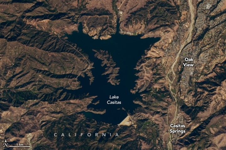 Lake Castias appears as a dark void in the image center. mountain peaks surround, more on the left side of the lake than the right. On the right the towns of Oak View and Casitas Springs appear to run vertically along the edge of a a riverbed.