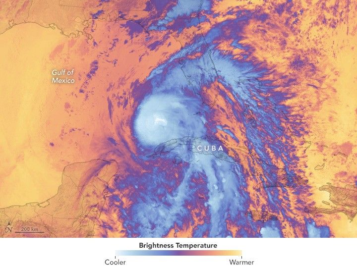 The temperature gradient image shows cool areas in shades of blue and warm in orange. The center of the image shows cool blue swirling clouds of a hurricane, with the outer bands appearing more purple, surrounded by warm bright orange colored ocean and land