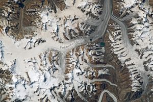 The Fedchenko Glacier and snow fields that contribute to it are visible, interspersed with mountain peaks. There is a small cloud and it's shadow near the image center, both over the glacier. On the top left is a debris covered glacier and the top right is where the Fedchenko Glacier exits the image. Within that region are two distinct dark lines labelled Moraines
