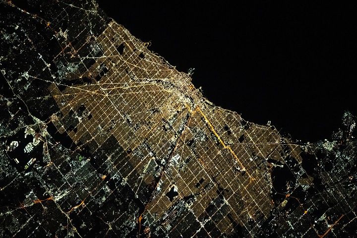Orange, yellow, and white lights span Chicago at night, illuminating its gridded downtown and tracing its sinuous rivers and parks.