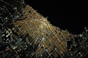 Orange, yellow, and white lights span Chicago at night, illuminating its gridded downtown and tracing its sinuous rivers and parks.